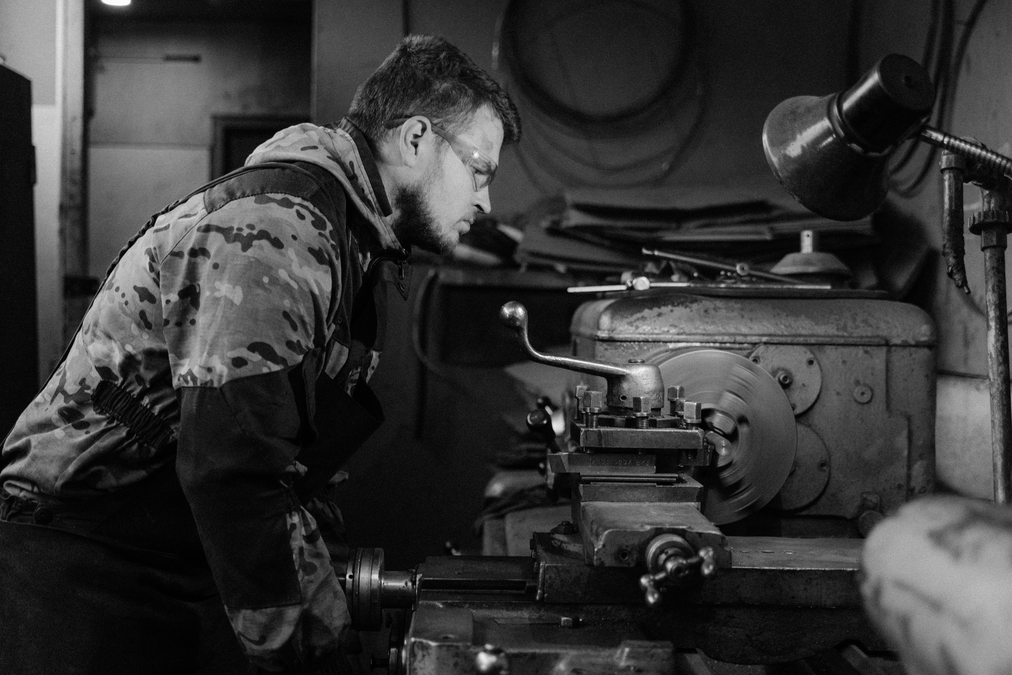 Black-and-white photograph of a worker operating a lathe in a workshop